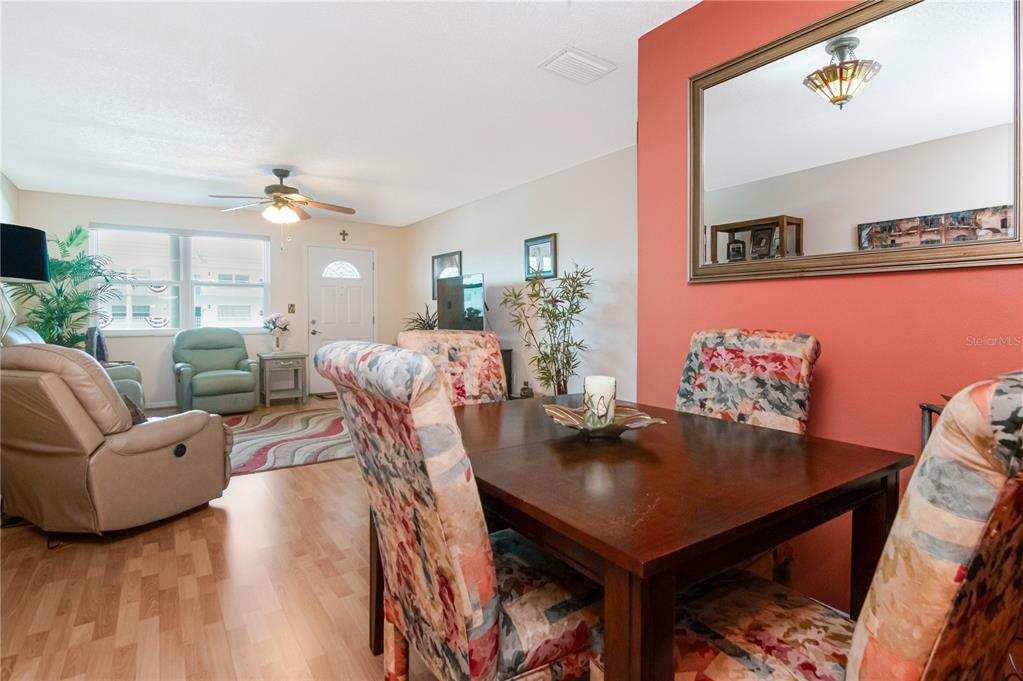 A dining area with floral chairs sits in front of a living room with light flooring — 5935 30TH AVENUE S UNIT 206, GULFPORT, FL
