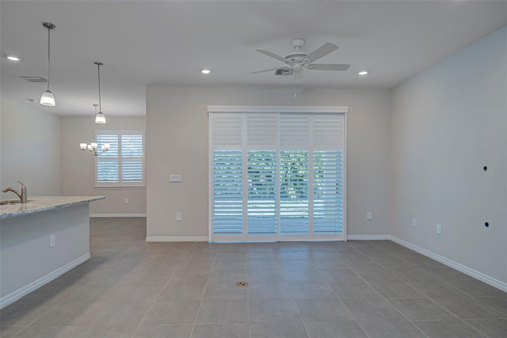 A bright, open-concept room features gray tile flooring, a ceiling fan, and sliding glass doors — 7416 S MOSS ROSE, PUNTA GORDA, FL