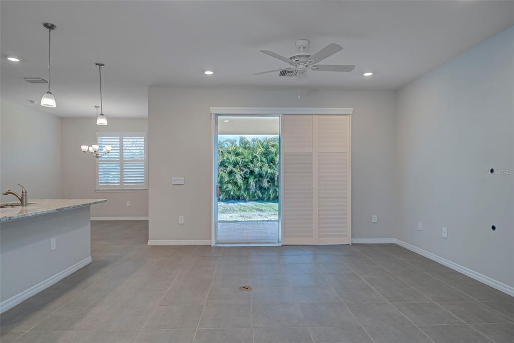 A bright, open-concept living area features gray tile flooring, a ceiling fan, and sliding doors — 7416 S MOSS ROSE, PUNTA GORDA, FL
