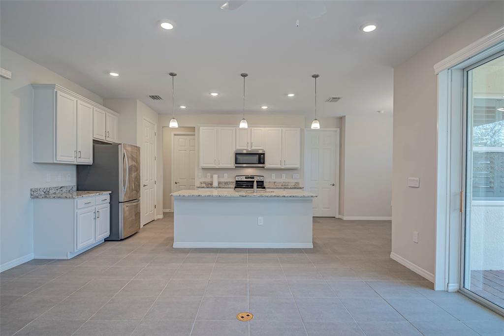 A kitchen features white cabinets, granite countertops, stainless steel appliances, and gray tile flooring — 7416 S MOSS ROSE, PUNTA GORDA, FL