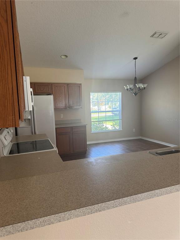 A kitchen with wood cabinets, white appliances, and a breakfast bar overlooking a dining area — 606 TAMARIN LANE, KISSIMMEE, FL