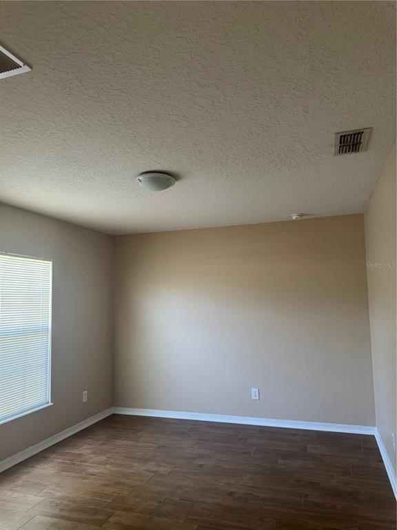 An empty room features beige walls, dark wood-look flooring, a ceiling light, and a window — 606 TAMARIN LANE, KISSIMMEE, FL