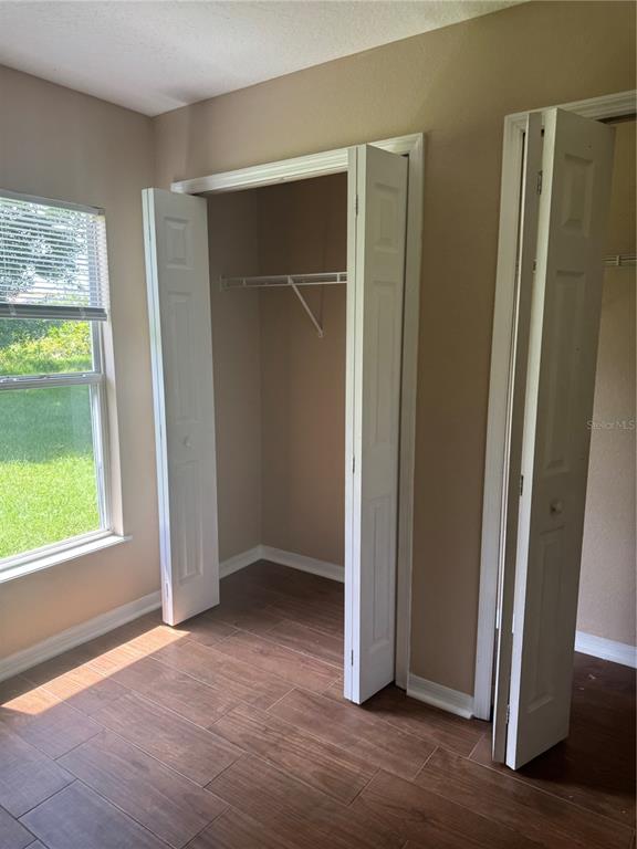 A room with wood-look tile flooring, a window, and two open white bi-fold closet doors — 606 TAMARIN LANE, KISSIMMEE, FL