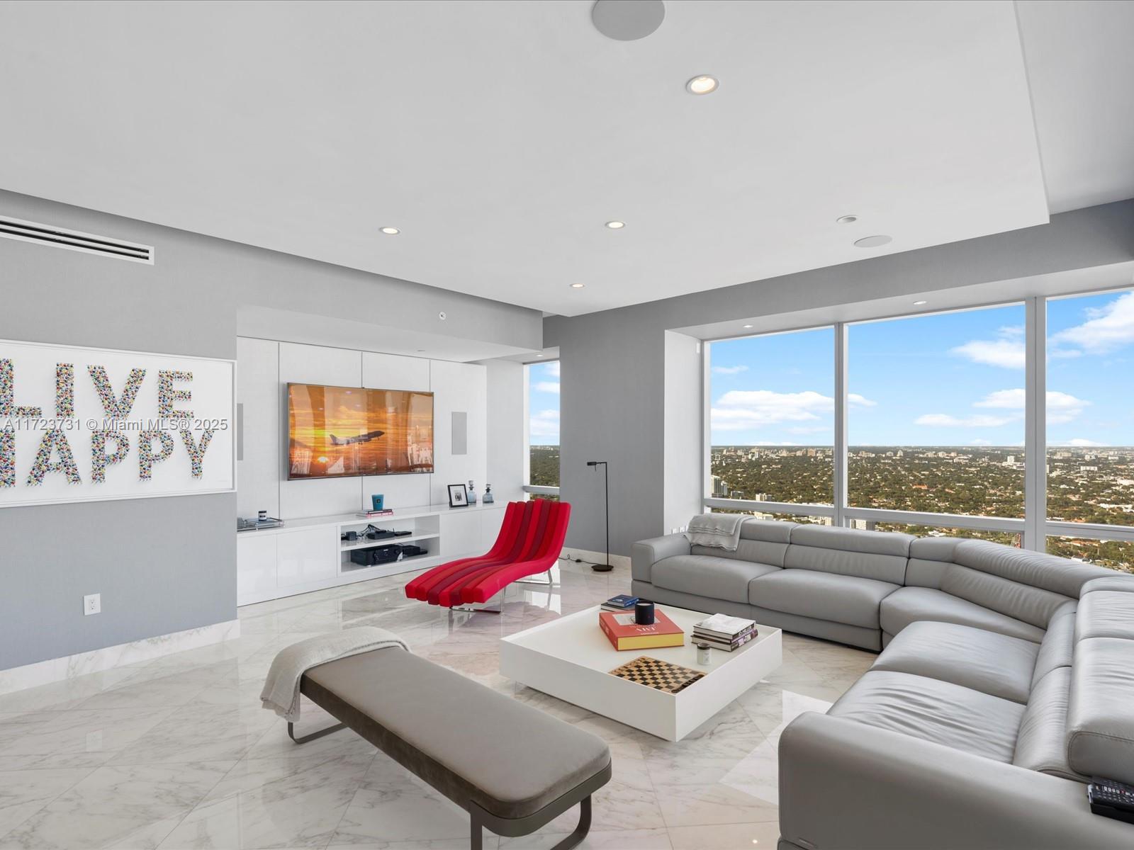 A modern living room features a grey sectional sofa, red lounge chair, and floor-to-ceiling windows — 1425 Brickell Ave, Miami FL 33131, MIAMI, FL