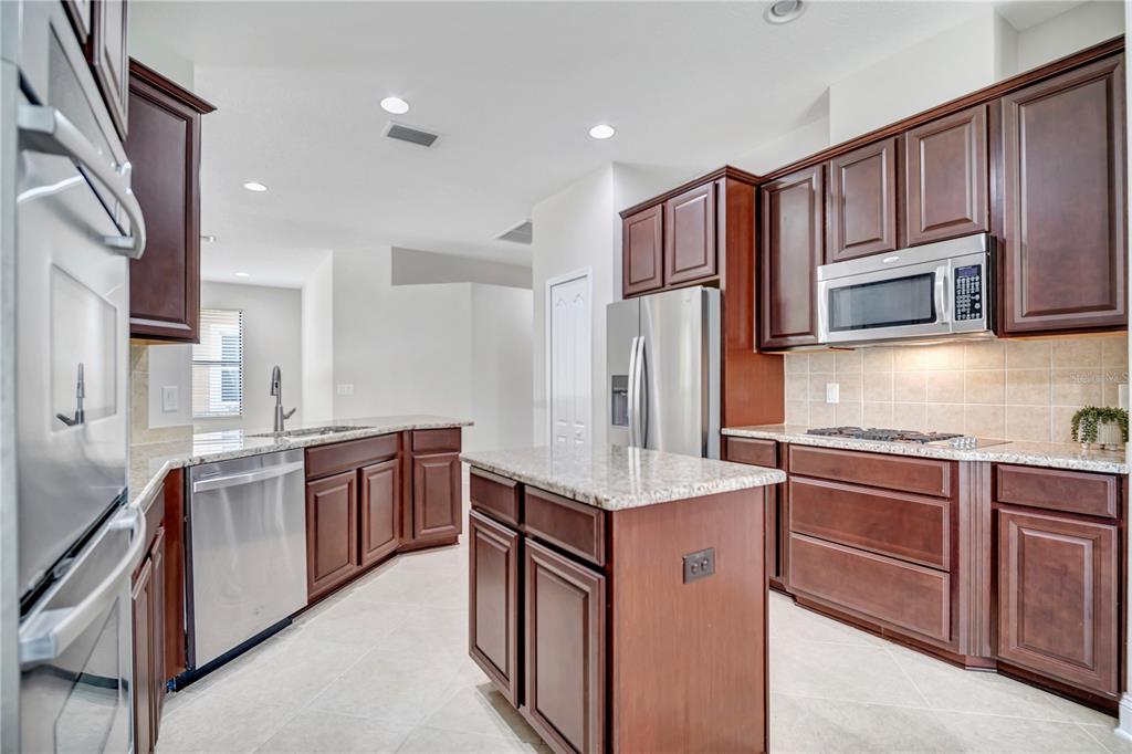 A kitchen features dark wood cabinets, granite countertops, stainless steel appliances, and a central island — 8013 HAMPTON GLEN DRIVE, TAMPA, FL