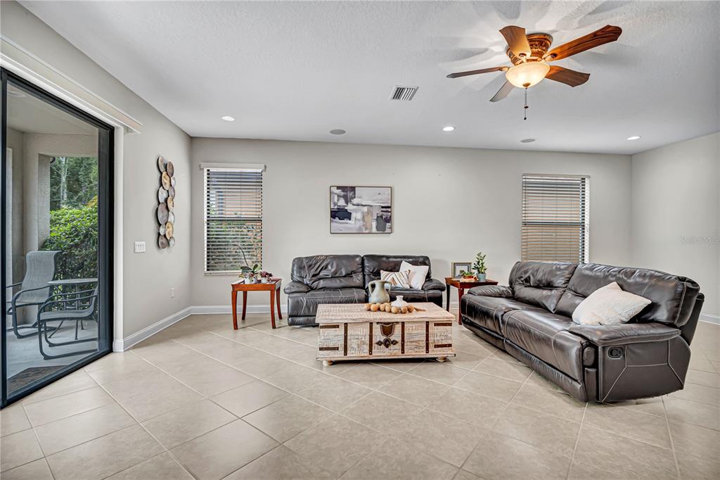 A living room features tile flooring, two dark leather sofas, a coffee table, and ceiling fan — 8013 HAMPTON GLEN DRIVE, TAMPA, FL