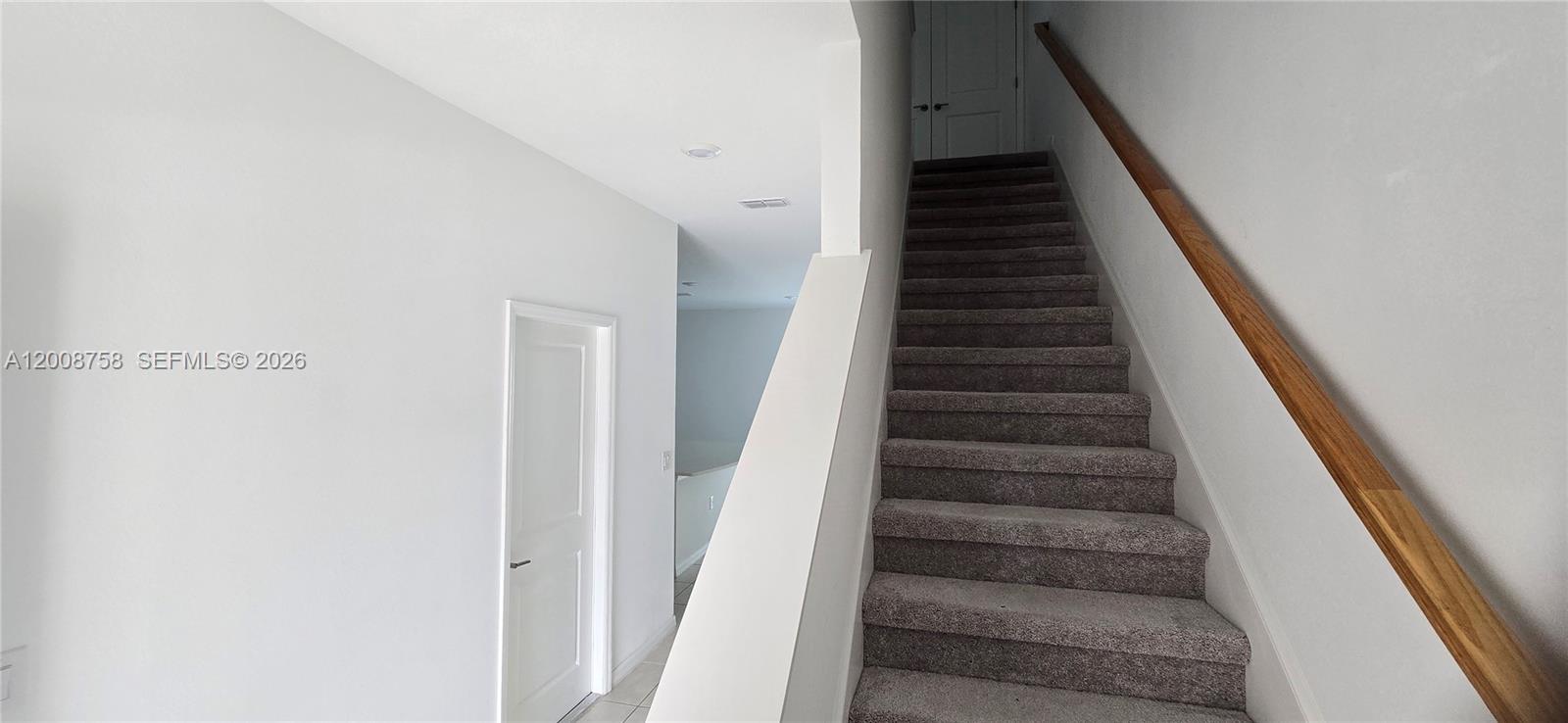 A carpeted staircase with a wooden handrail leads to a landing with a white door — 2978 Canary Ave, Davenport FL 33837, DAVENPORT, FL