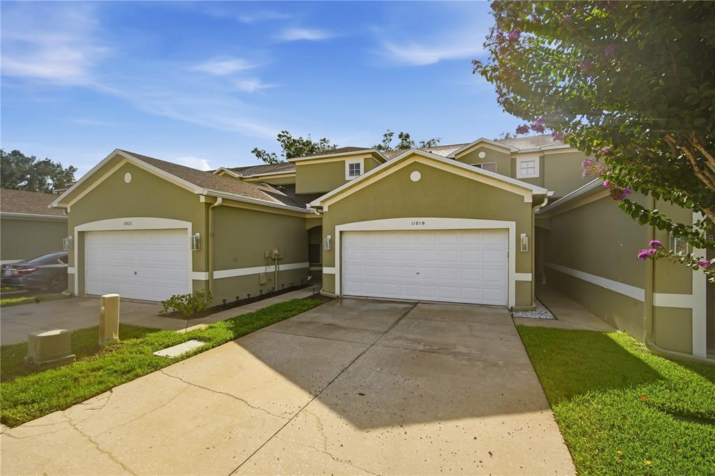 A two-story duplex with green stucco siding, white garage doors, and concrete driveways — 11019 BLAINE TOP PLACE, TAMPA, FL