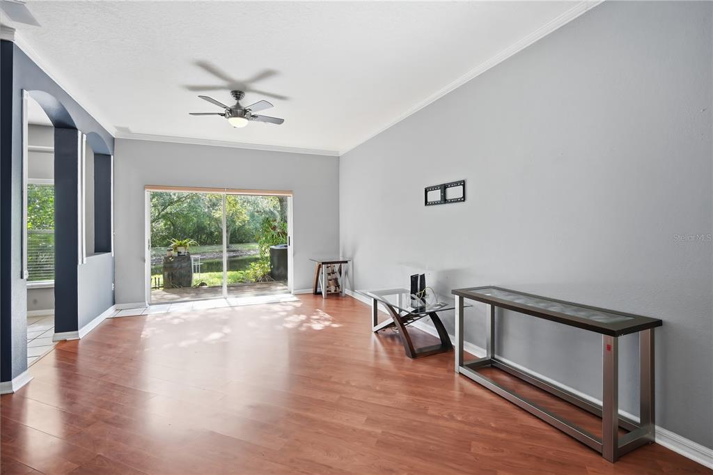 A living room with wood-look flooring, a ceiling fan, and sliding glass doors to a patio — 11019 BLAINE TOP PLACE, TAMPA, FL