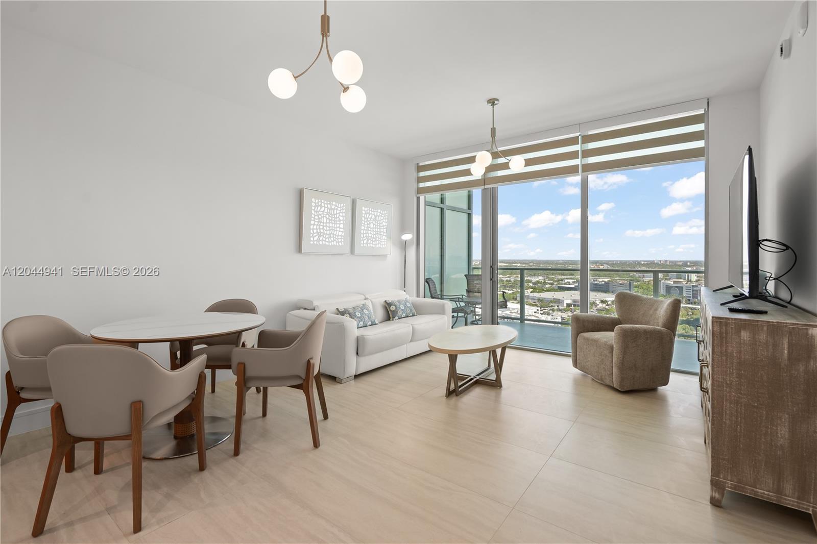 A modern living and dining area features floor-to-ceiling windows with a balcony and city view — 2411 Laguna Circle # 2107, Miami FL 33181, MIAMI, FL
