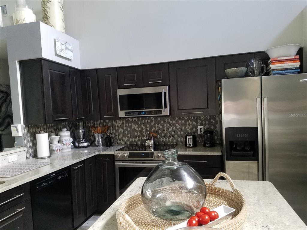 A kitchen features dark wood cabinets, stainless steel appliances, a patterned backsplash, and granite countertops — 15211 ARBOR HOLLOW DRIVE, ODESSA, FL