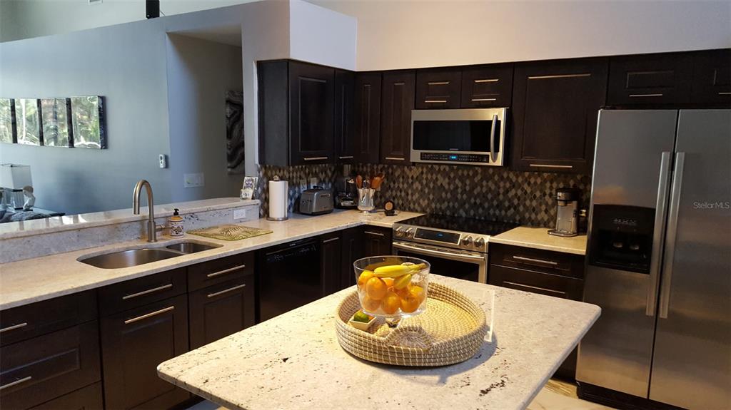 A kitchen features dark wood cabinets, granite countertops, stainless steel appliances, and a central island — 15211 ARBOR HOLLOW DRIVE, ODESSA, FL