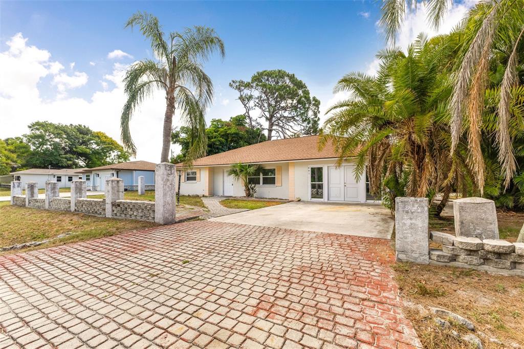 A single-story house with a brick paver driveway, palm trees, and a stone perimeter wall — 887 LEEWARD ROAD, VENICE, FL