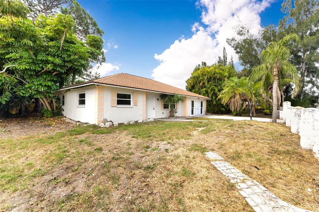 A single-story house with a white exterior, tan shutters, and a brown shingled roof — 887 LEEWARD ROAD, VENICE, FL