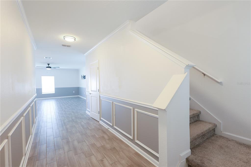 A hallway with wood-look tile flooring, wainscoting, and a carpeted staircase leading upward — 1821 HEART LAKE DRIVE, GROVELAND, FL