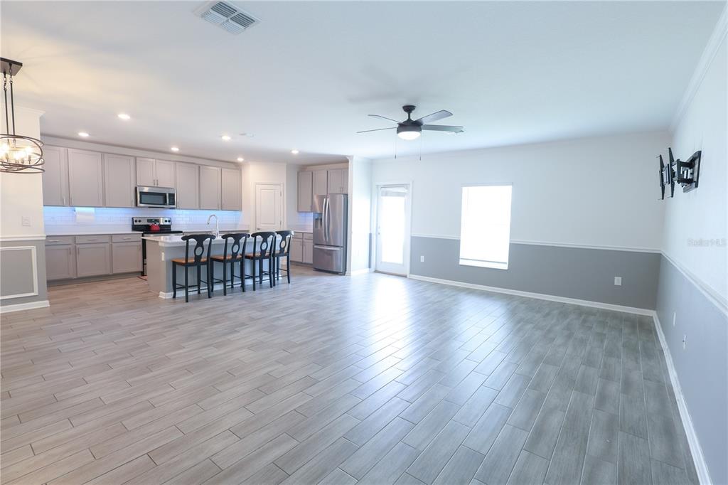 An open-concept kitchen and living area features gray cabinetry, stainless appliances, and wood-look tile flooring — 1821 HEART LAKE DRIVE, GROVELAND, FL