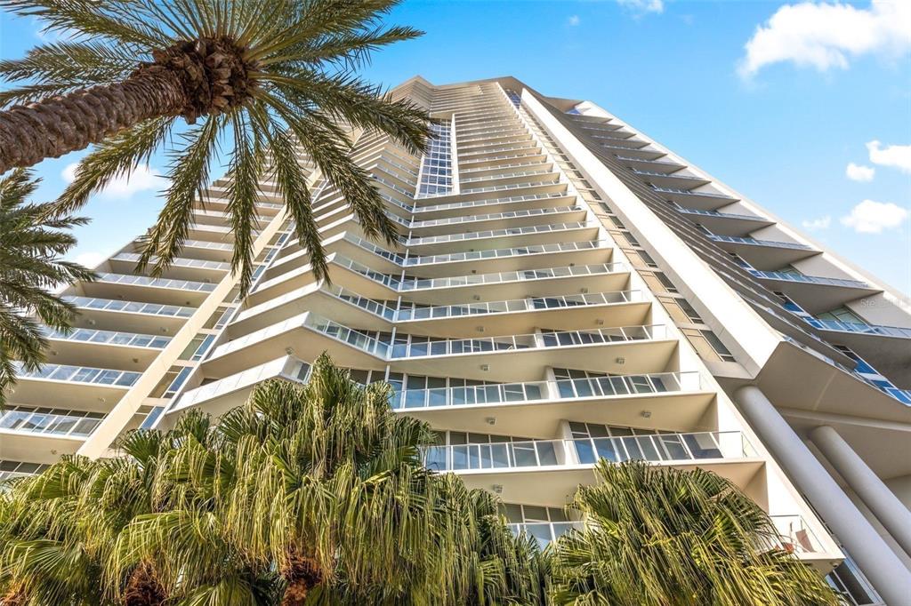 A low-angle view of a modern high-rise building with balconies framed by palm trees — 175 1ST STREET S UNIT 3102, ST PETERSBURG, FL