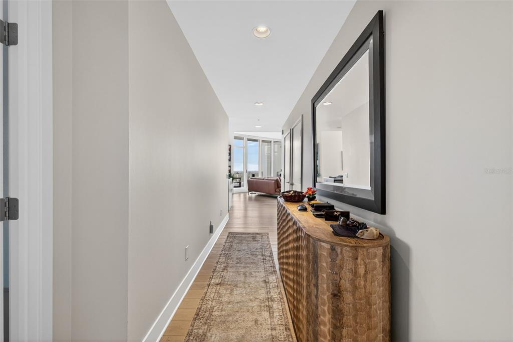 A hallway with light wood floors, a textured wooden console table, and a large wall mirror — 175 1ST STREET S UNIT 3102, ST PETERSBURG, FL