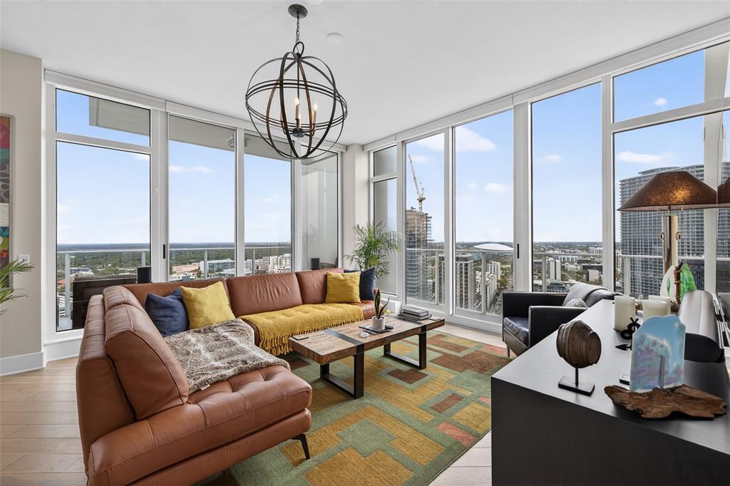 A modern living room features a brown leather sectional, floor-to-ceiling windows, and city views — 175 1ST STREET S UNIT 3102, ST PETERSBURG, FL