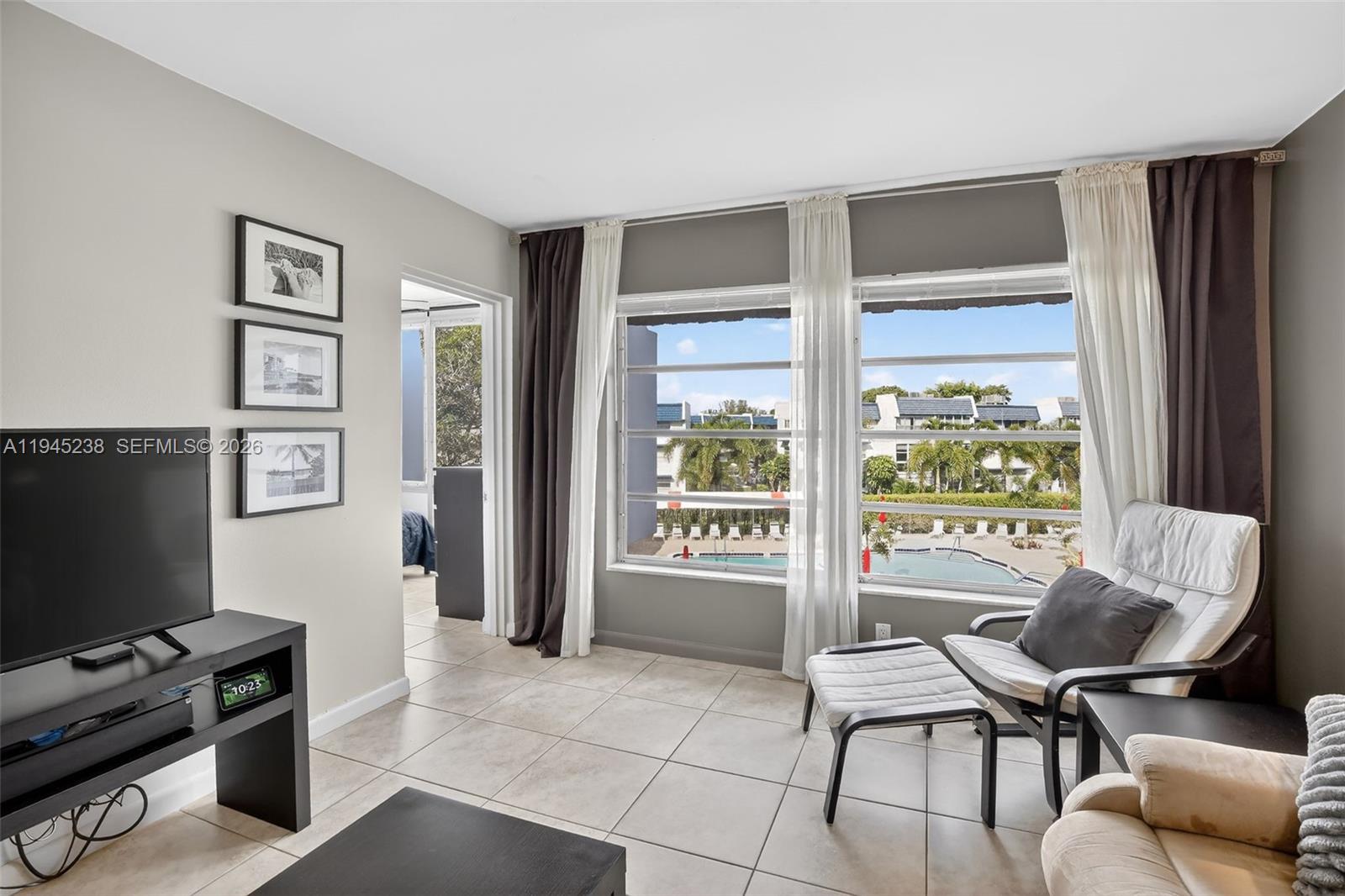 A living room features tile floors, a television, and large windows overlooking a swimming pool — 7897 Golf Circle Dr # 307, Margate FL 33063, MARGATE, FL
