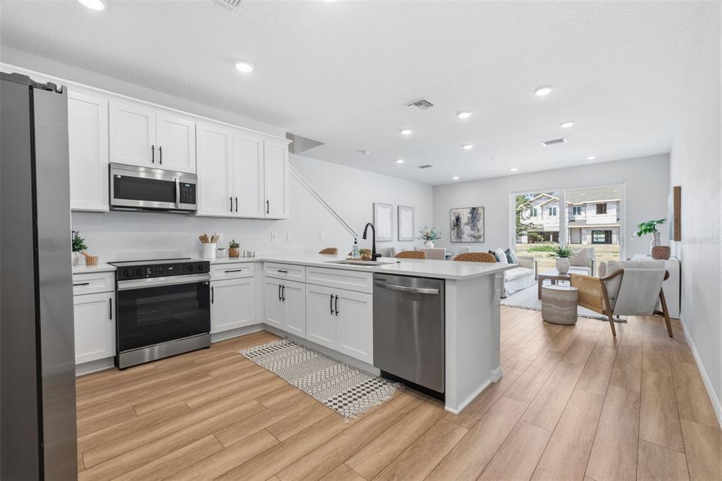 A modern kitchen with white cabinets and stainless steel appliances opens to a living area — 5831 JACKIE MAE PLACE, RIVERVIEW, FL