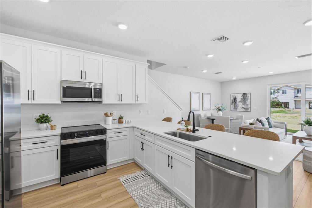 A modern kitchen features white cabinets, stainless steel appliances, and a large quartz island — 5831 JACKIE MAE PLACE, RIVERVIEW, FL