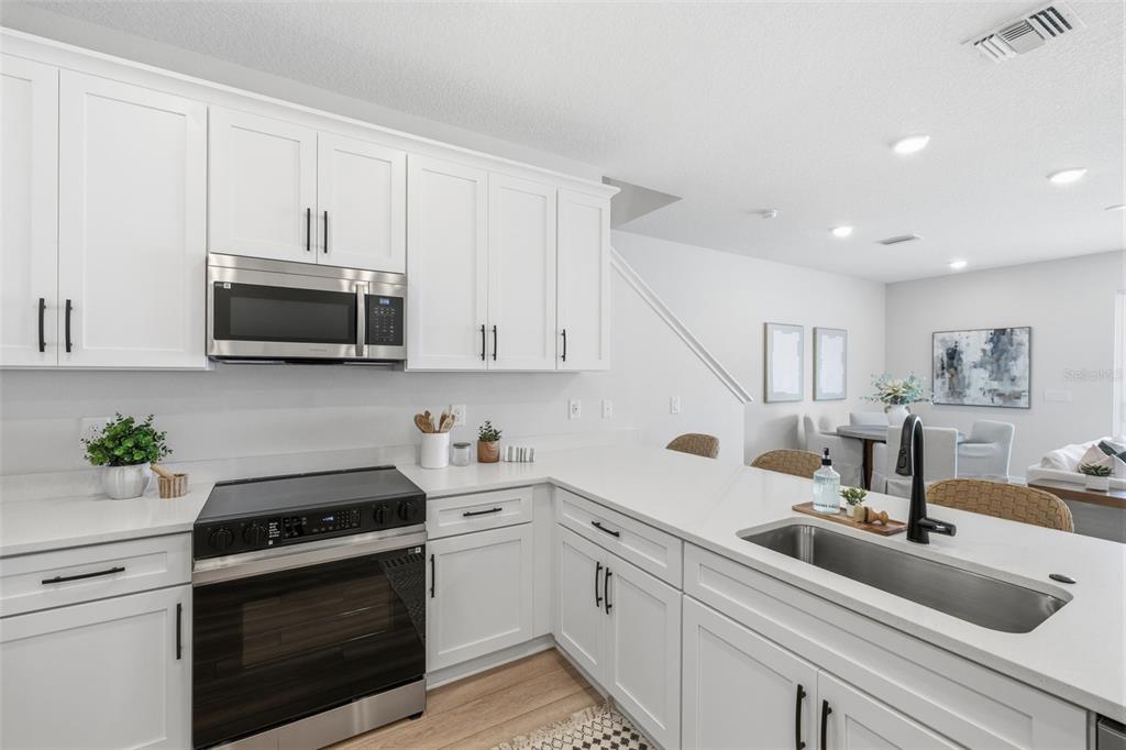 A modern kitchen features white cabinets, stainless steel appliances, and a quartz countertop island — 5831 JACKIE MAE PLACE, RIVERVIEW, FL