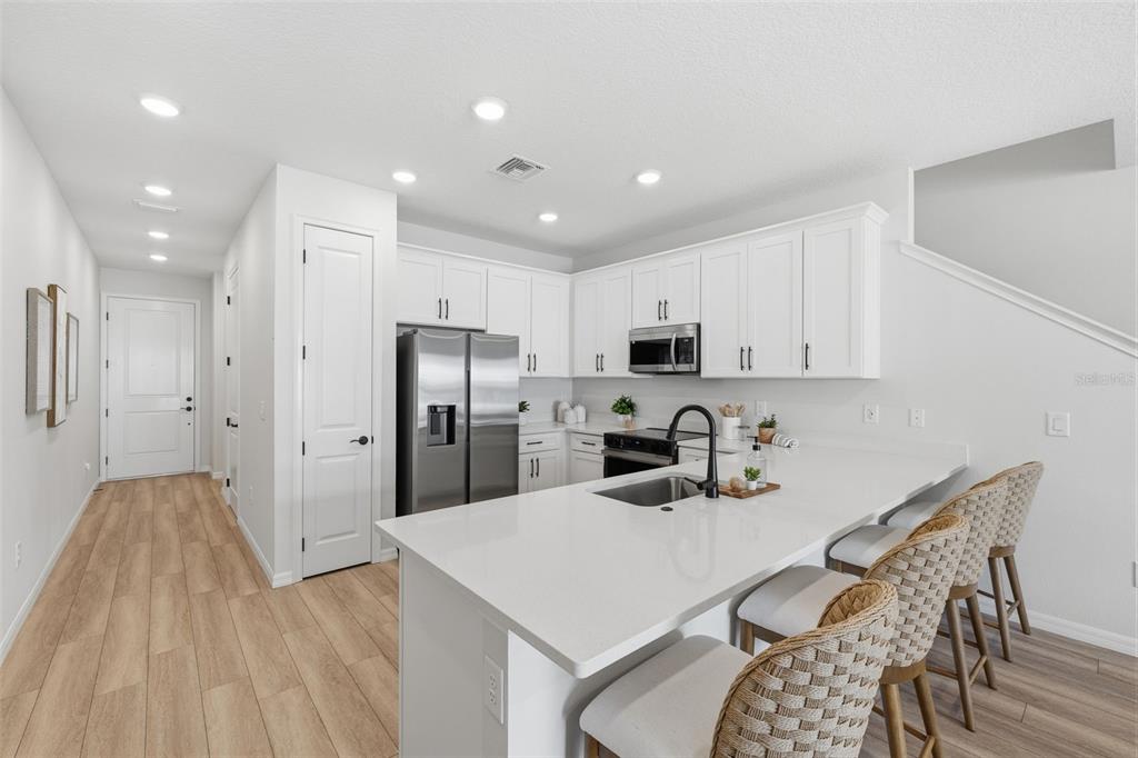 A modern kitchen features white cabinetry, stainless steel appliances, and a quartz-topped island with seating — 5831 JACKIE MAE PLACE, RIVERVIEW, FL