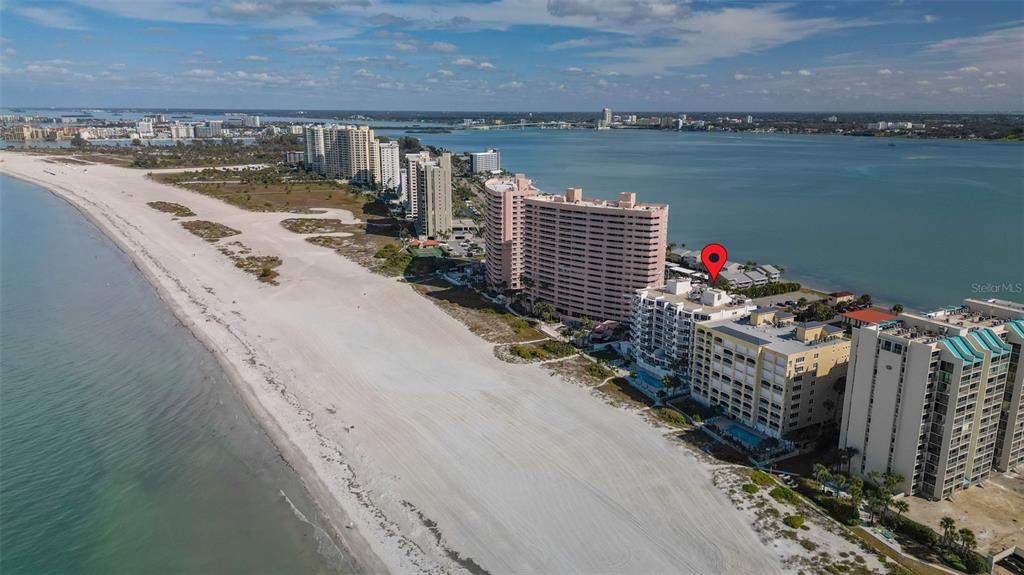 An aerial view shows high-rise condominiums situated along a sandy beach and coastal water — 1350 GULF BOULEVARD UNIT 704, CLEARWATER BEACH, FL
