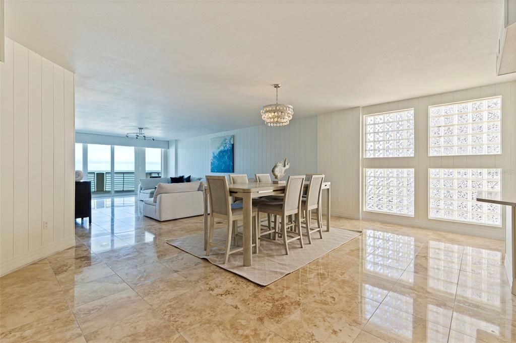 A dining area with a chandelier and glass block windows sits beside a living room — 1350 GULF BOULEVARD UNIT 704, CLEARWATER BEACH, FL