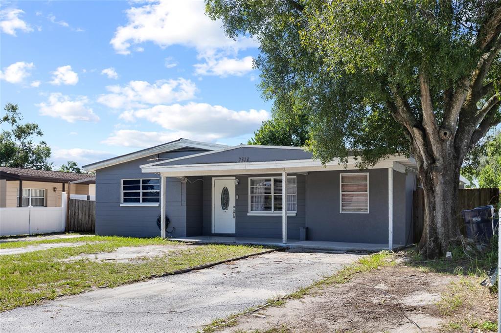 A single-story gray house with a covered front porch and a large tree in front — 2313 E 111TH AVE, TAMPA, FL