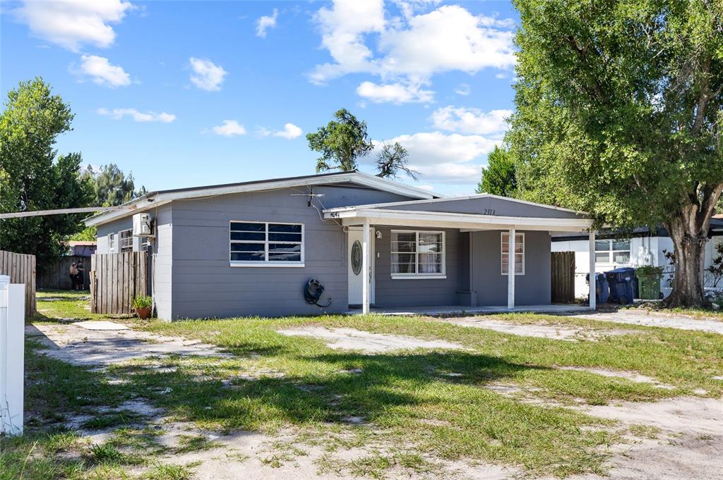 A gray, single-story house with a covered front porch and a large, unpaved front yard — 2313 E 111TH AVE, TAMPA, FL