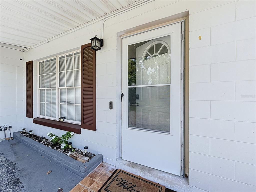 A white front door with a storm door sits beside a window with brown shutters — 7511 BROCKBANK DRIVE, ORLANDO, FL