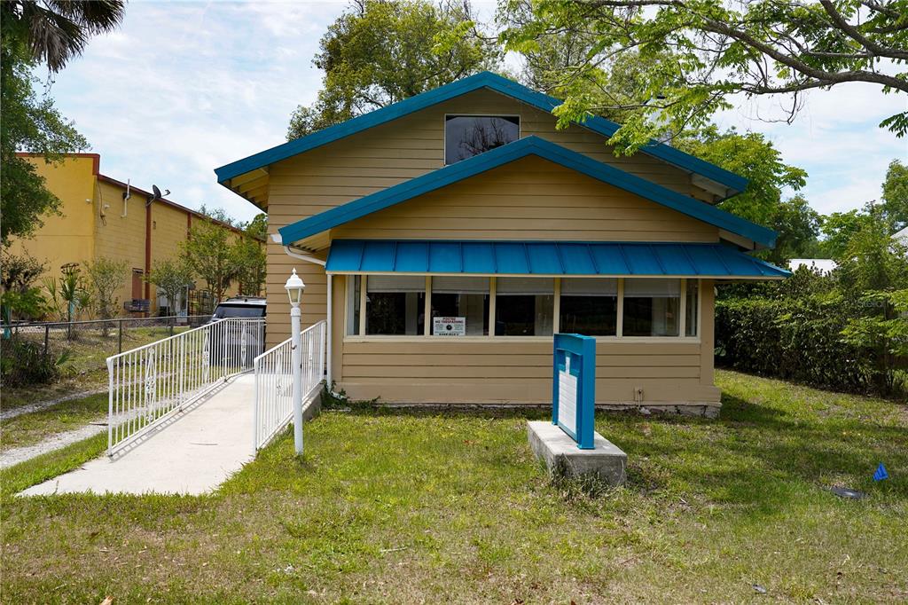A tan house with a blue metal roof and a white wheelchair ramp in front — 1004 TALTON AVENUE, DELAND, FL