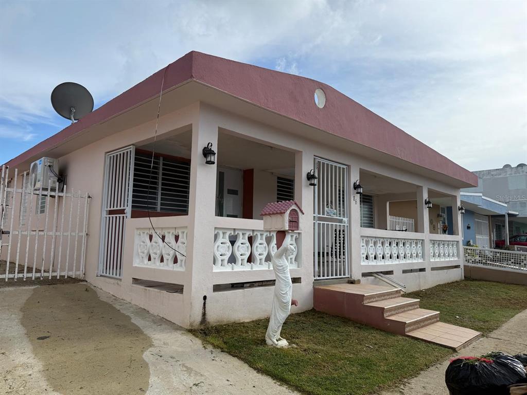 A pink single-story house features a covered porch, white decorative railings, and a mailbox statue — CALLE 8 BRISAS DE CEIBA UNIT 86, CEIBA, PR
