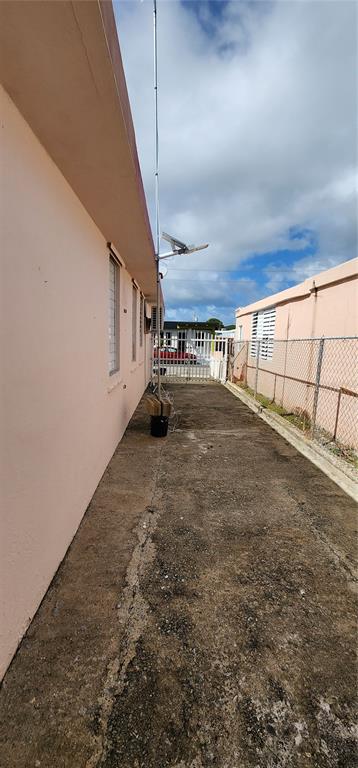 A narrow concrete side yard between two pink buildings features a tall metal antenna pole — CALLE 8 BRISAS DE CEIBA UNIT 86, CEIBA, PR