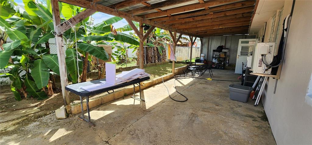 A covered concrete patio features a folding table, banana plants, and an outdoor air conditioner — CALLE 8 BRISAS DE CEIBA UNIT 86, CEIBA, PR
