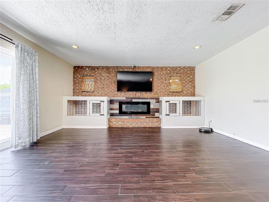 A living room features a brick fireplace wall, built-in dog crates, and dark wood-look flooring — 33 S ORTMAN DRIVE, ORLANDO, FL
