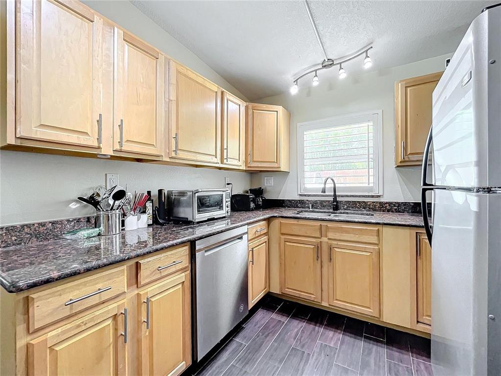 A kitchen features light wood cabinets, dark granite countertops, stainless steel appliances, and tile flooring — 33 S ORTMAN DRIVE, ORLANDO, FL