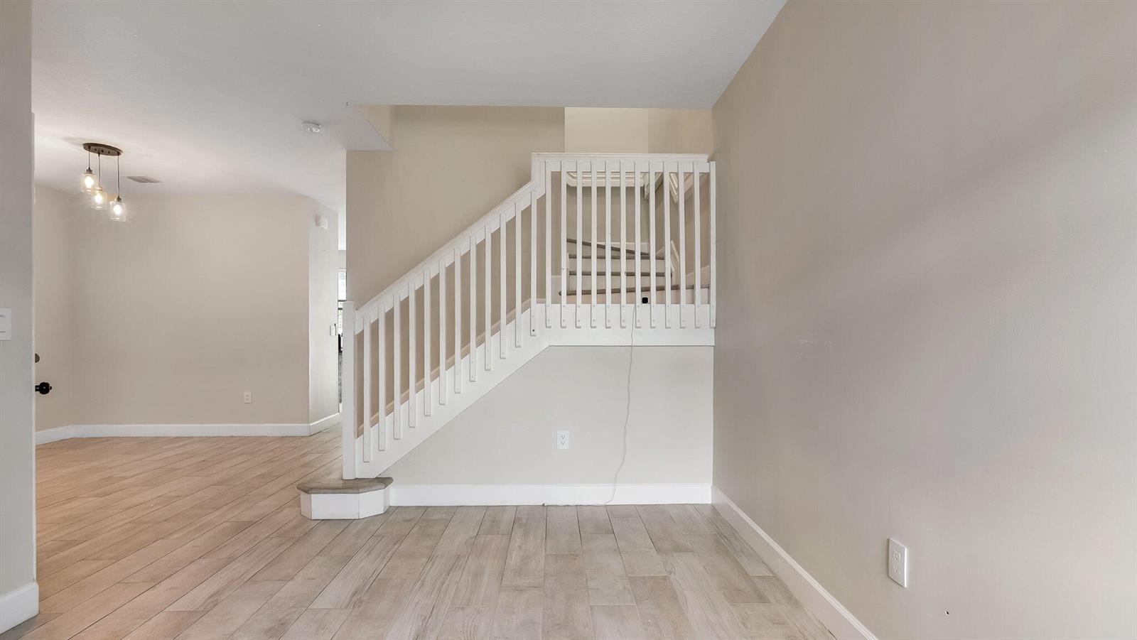 A room with light wood-look flooring, beige walls, and a white staircase with railings — 4805 NW 48th Terrace, Tamarac FL 33319, TAMARAC, FL