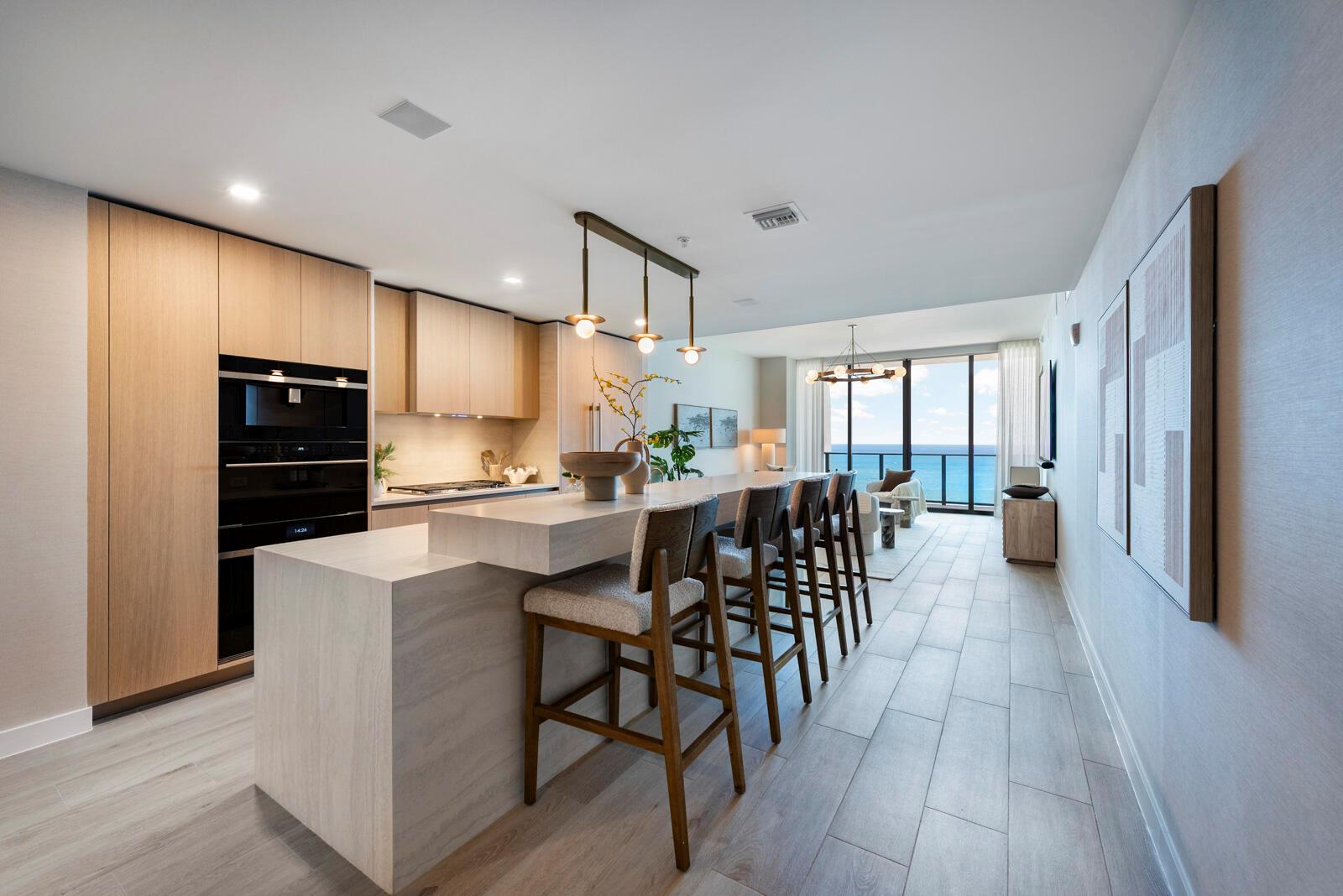 A modern kitchen features light wood cabinetry, a stone island with bar seating, and ocean views — 900 N Ocean Boulevard, Pompano Beach FL 33062, POMPANO BEACH, FL