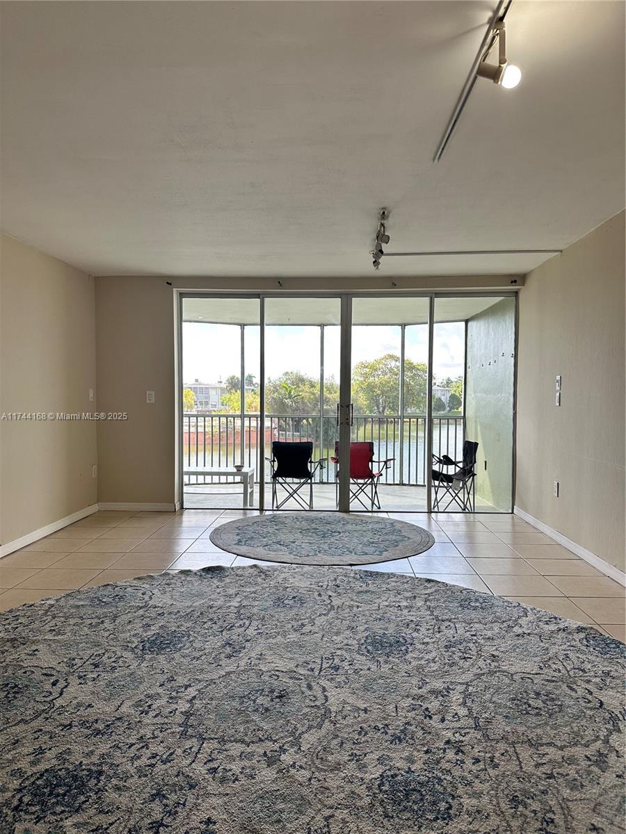 A living room with tile flooring, two circular rugs, and sliding glass doors leading to a balcony — 1750 NE 191st St # 4, Miami FL 33179, MIAMI, FL