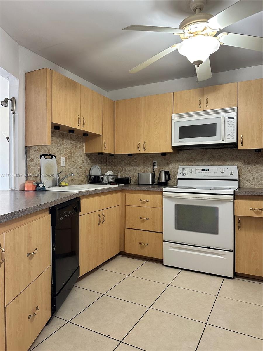 A kitchen features light wood cabinets, a white stove, a black dishwasher, and tiled flooring — 1750 NE 191st St # 4, Miami FL 33179, MIAMI, FL