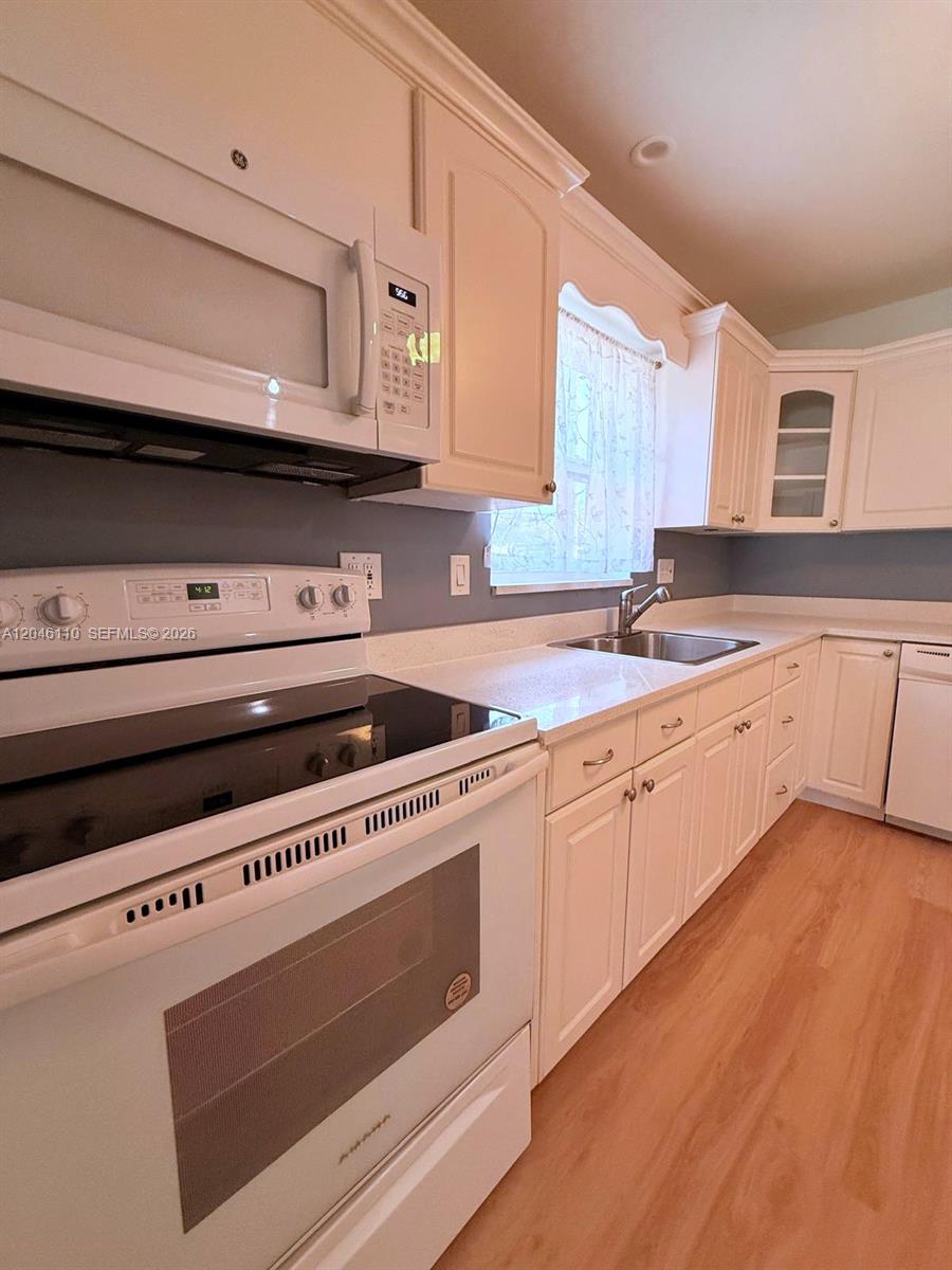 A kitchen features white cabinetry, a white stove, a microwave, and a stainless steel sink — 2832 Fillmore St # 20, Hollywood FL 33020, HOLLYWOOD, FL