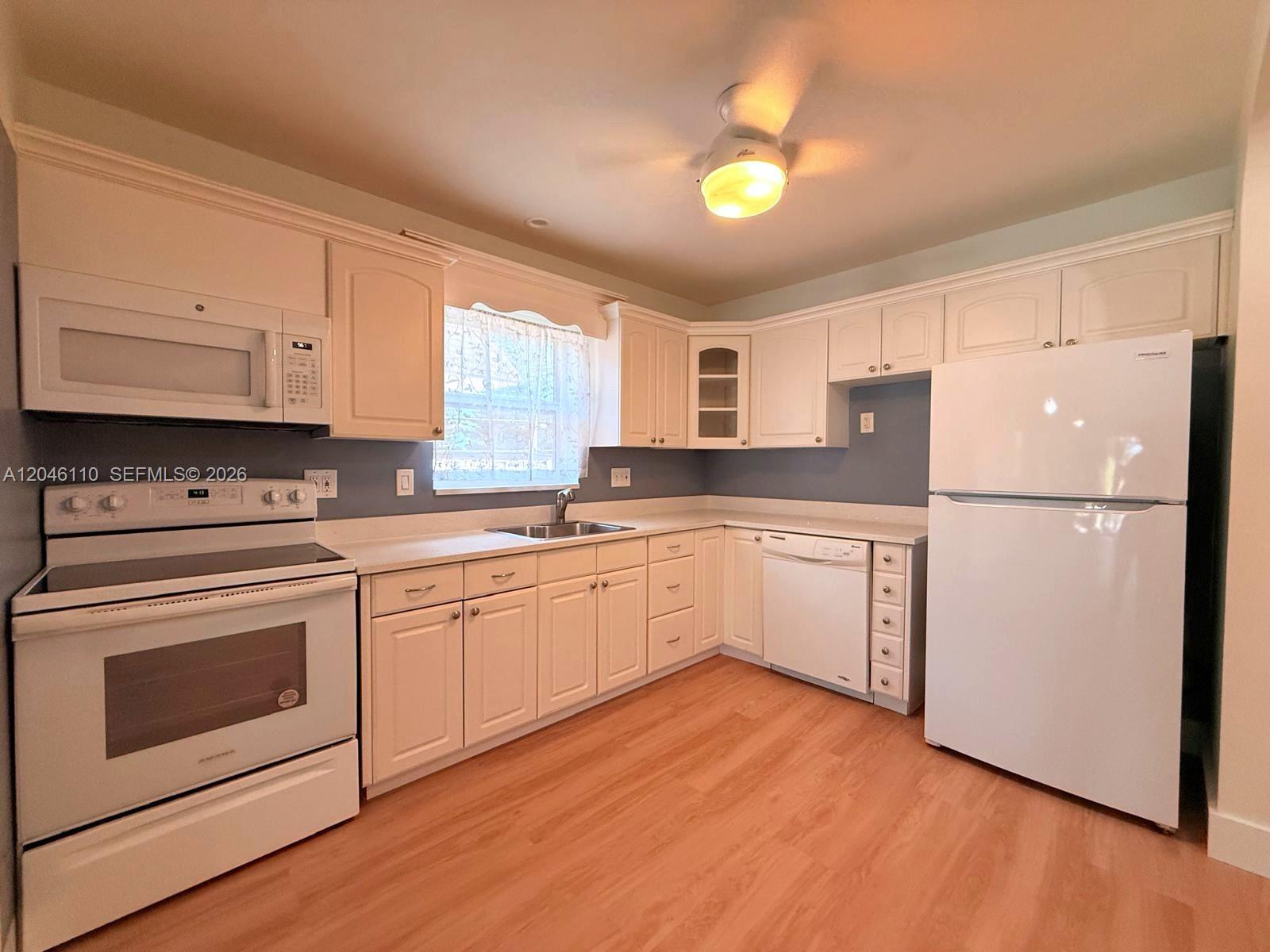 A kitchen features white cabinets, white appliances, a window, and light wood-look flooring — 2832 Fillmore St # 20, Hollywood FL 33020, HOLLYWOOD, FL