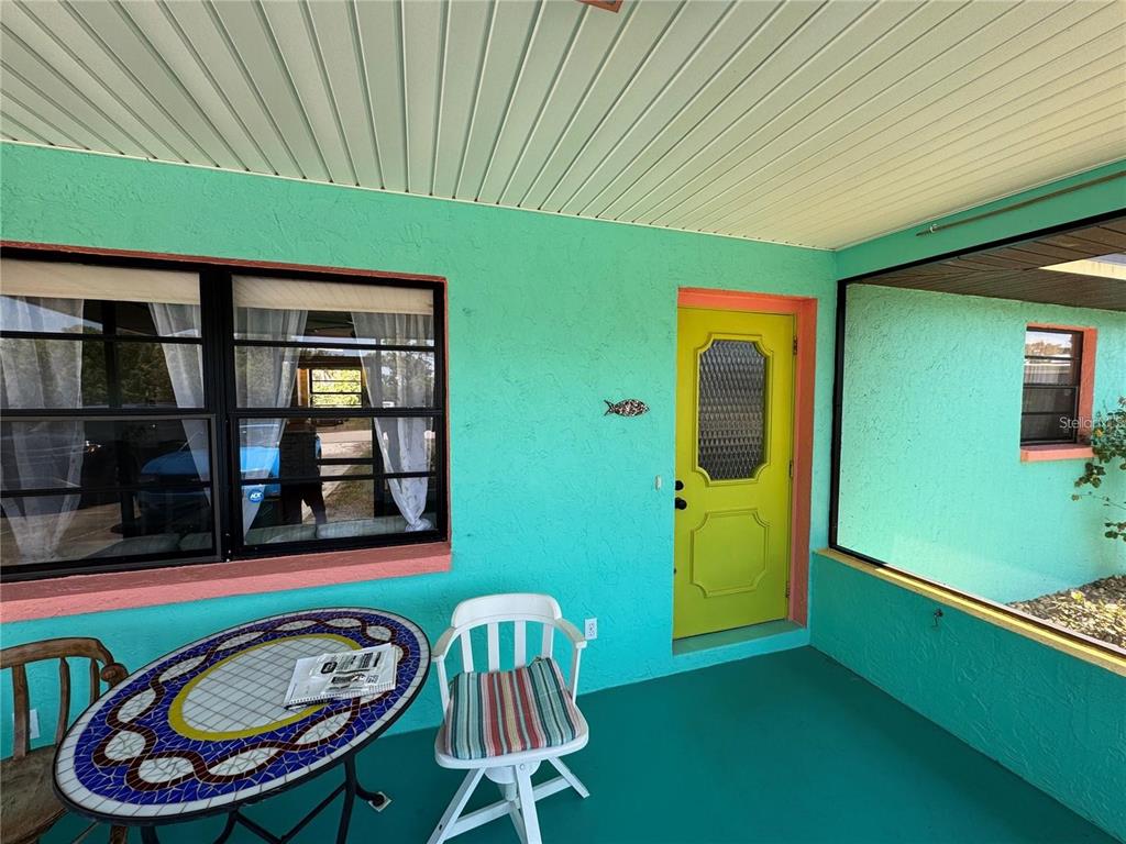 A covered porch with bright turquoise walls, a yellow door, and a mosaic-topped table — 3141 10TH STREET, ENGLEWOOD, FL