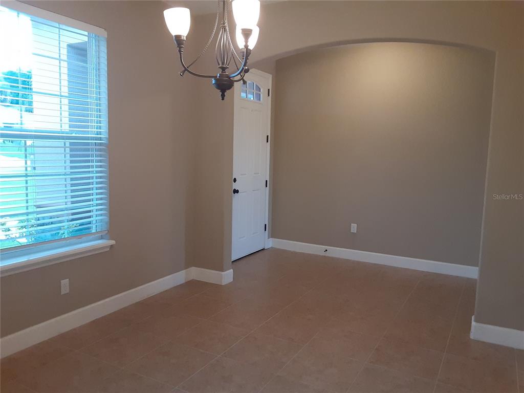 A dining room features tile flooring, a chandelier, a window with blinds, and an arched wall — 33848 EMERALD POND LOOP, LEESBURG, FL