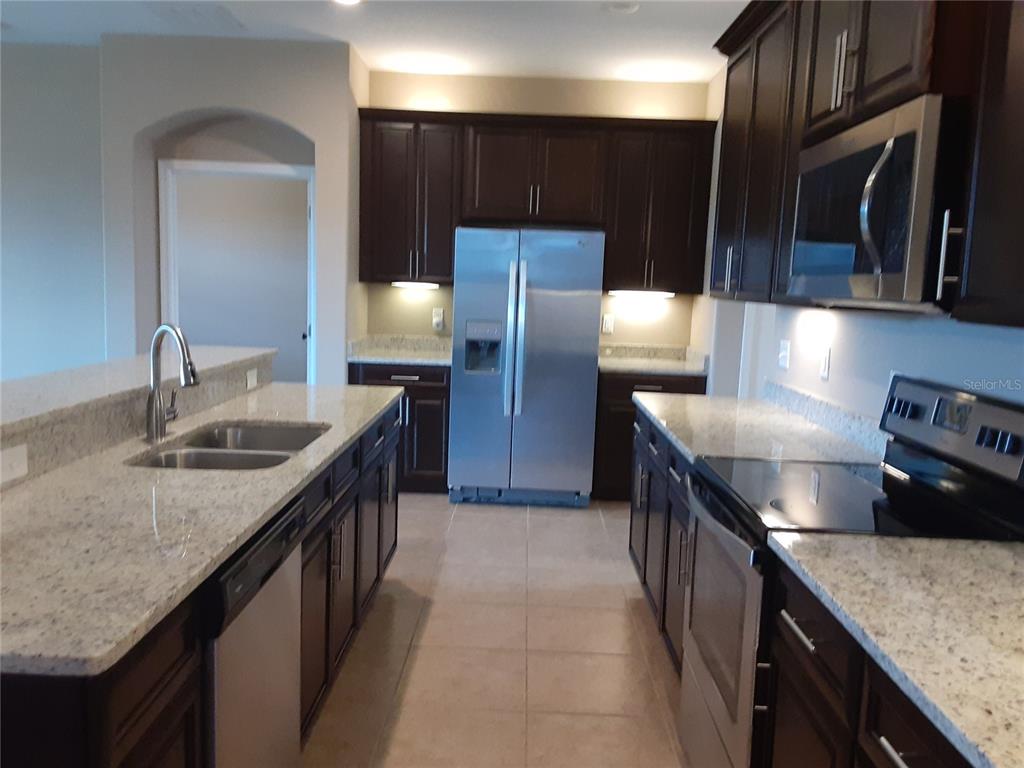 A kitchen features dark wood cabinets, granite countertops, stainless steel appliances, and a central island — 33848 EMERALD POND LOOP, LEESBURG, FL