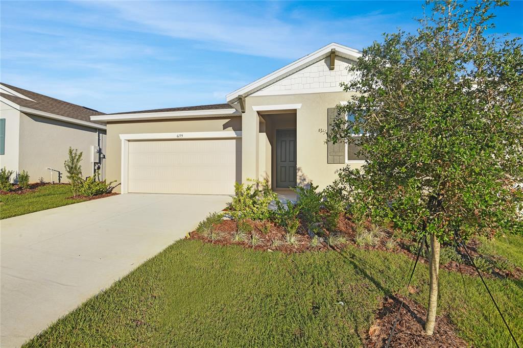A single-story suburban house with a tan stucco exterior, a two-car garage, and a front lawn — 6179 DAPHNE STREET, LAKE HAMILTON, FL