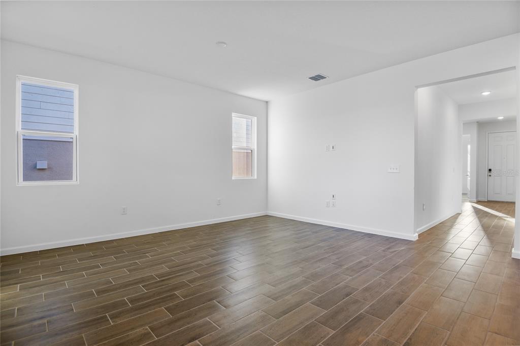 An empty living room features white walls, wood-look tile flooring, and two windows — 6179 DAPHNE STREET, LAKE HAMILTON, FL